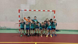 Drużyna UKS Lipusz rocznik 2009- w koszulkach o kolorze miętowym, bramkarze w kolorze pomarańczowym. Zdjęcie zrobione na tle bramki od piłki ręcznej.