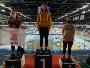 Trzy osoby stojące na podium w tle widać bieżnie lekkoatletyczną oraz trybuny