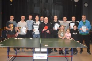 Ustawieni zawodnicy z dyplomami oraz pucharami oraz ksiądz Proboszcz w GOKSiR Lipusz po zakończeniu turnieju w tenisie stołowym