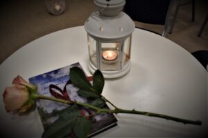 Zdjęcie na którym na książce wierszy gostomskich leży róża, obok latarenka