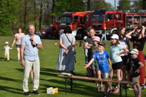 Zdjęcie przedstawia Dyrektora GOKSiR i innych ludzi podczas atrakcji, w tle wozy strażackie