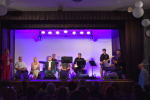 Zdjęcie przedstawia grupę muzyków na scenie, widać widownie