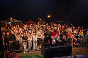 Zdjęcie przedstawia tłum ludzi pod barierkami unoszących ręce w góre, z tyłu widać namioty