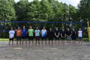 Na zdjęciu widać 12 zawodników siatkówki plażowej, którzy uczestniczyli w 3 turnieju siatkówki plażowej z cyklu Grand Prix Lipusza 2025, w tle siatka i zielone drzewa